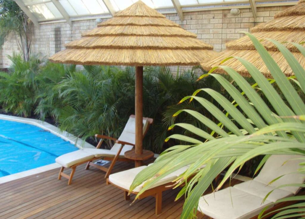 Outdoor living area by a pool with thatched umbrellas and deck chairs.