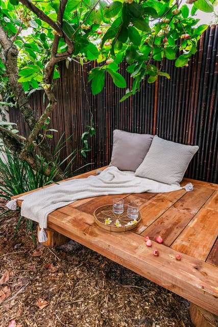 A rustic wooden bench placed centrally in a blooming garden with a bowl of 2 glasses of water.