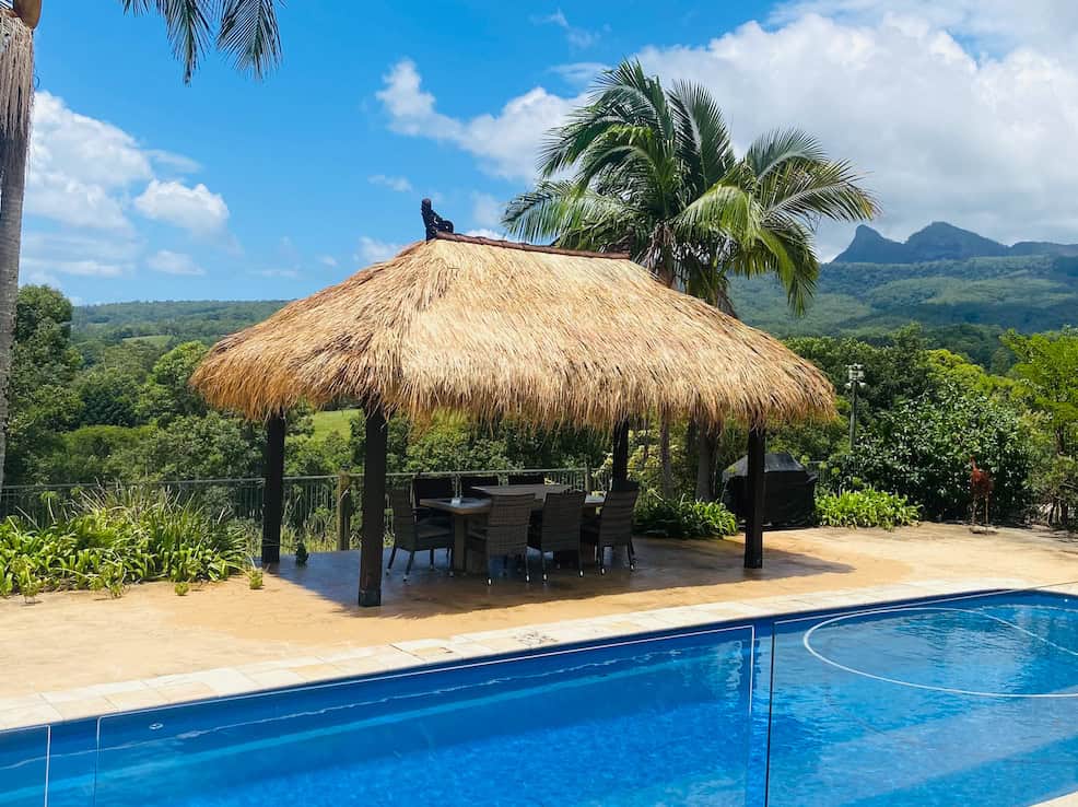 A serene pool with a bali thatched roof, accompanied by a table and chairs for relaxation.